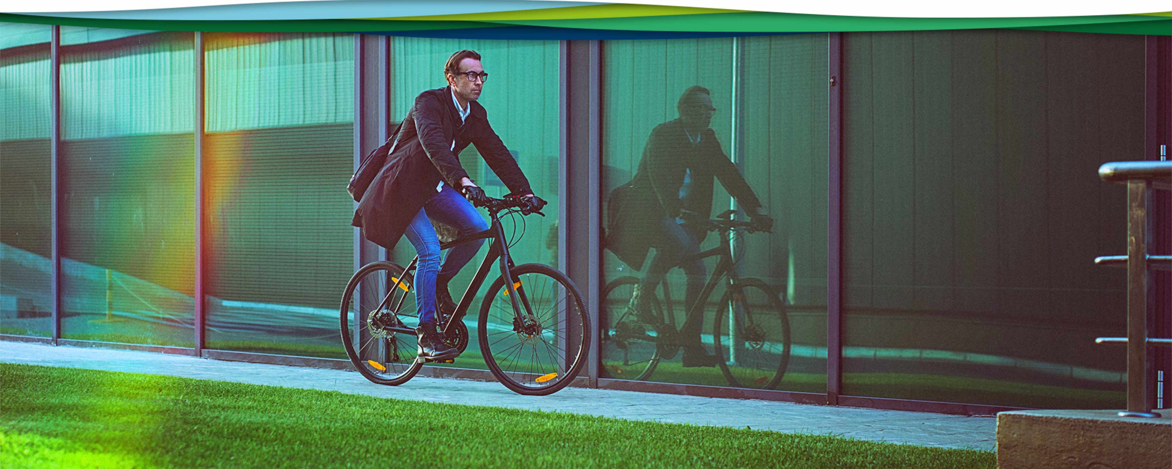 Business Tüp fährt Fahrrad vor Glasfassade
